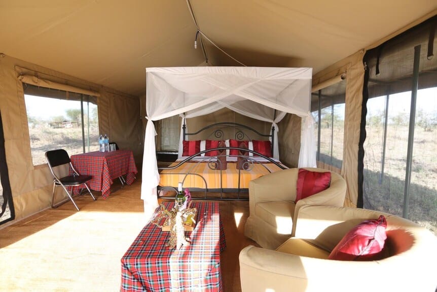 A four-poster bed with red throws inside a luxury safari tent