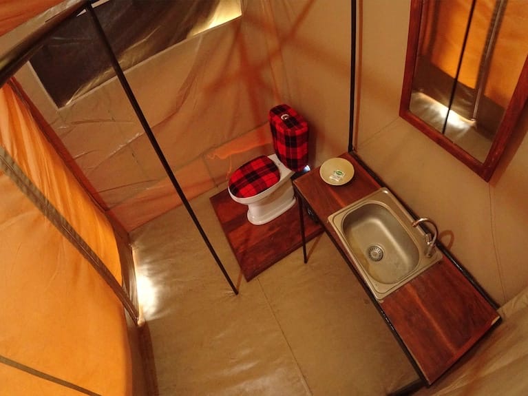 An en-suite bathroom inside a safari tent, with a Maasai blanket